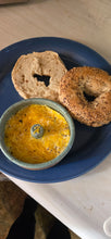 Load image into Gallery viewer, Handmade speckled green ceramic Eggle containing a ring-shaped cooked egg, served beside a sliced bagel on a blue plate.